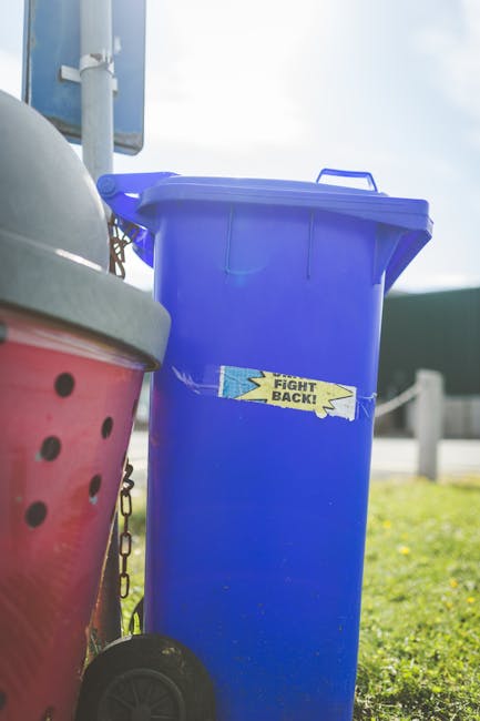 A person’s arm and hand are visible, holding a tightly knotted green plastic rubbish bag, which contains waste material and appears to be full. The bag's surface is partially semi-transparent, revea